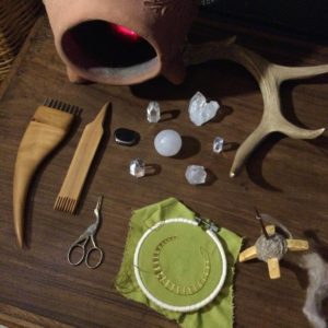 Weaving, spinning, and embroidery tools arranged with crystals and an antler.
